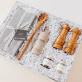 Load image into Gallery viewer, Lavender and Pine Entertainer's Kitchen Gift Box angle view featuring Kaf Home grey linen napkins, Le Marké olive oil, Natural OliveWood pasta spoon, Natural OliveWood salt and pepper mills, and La Boite grey salt and Tellicherry pepper in white magnetic gift box