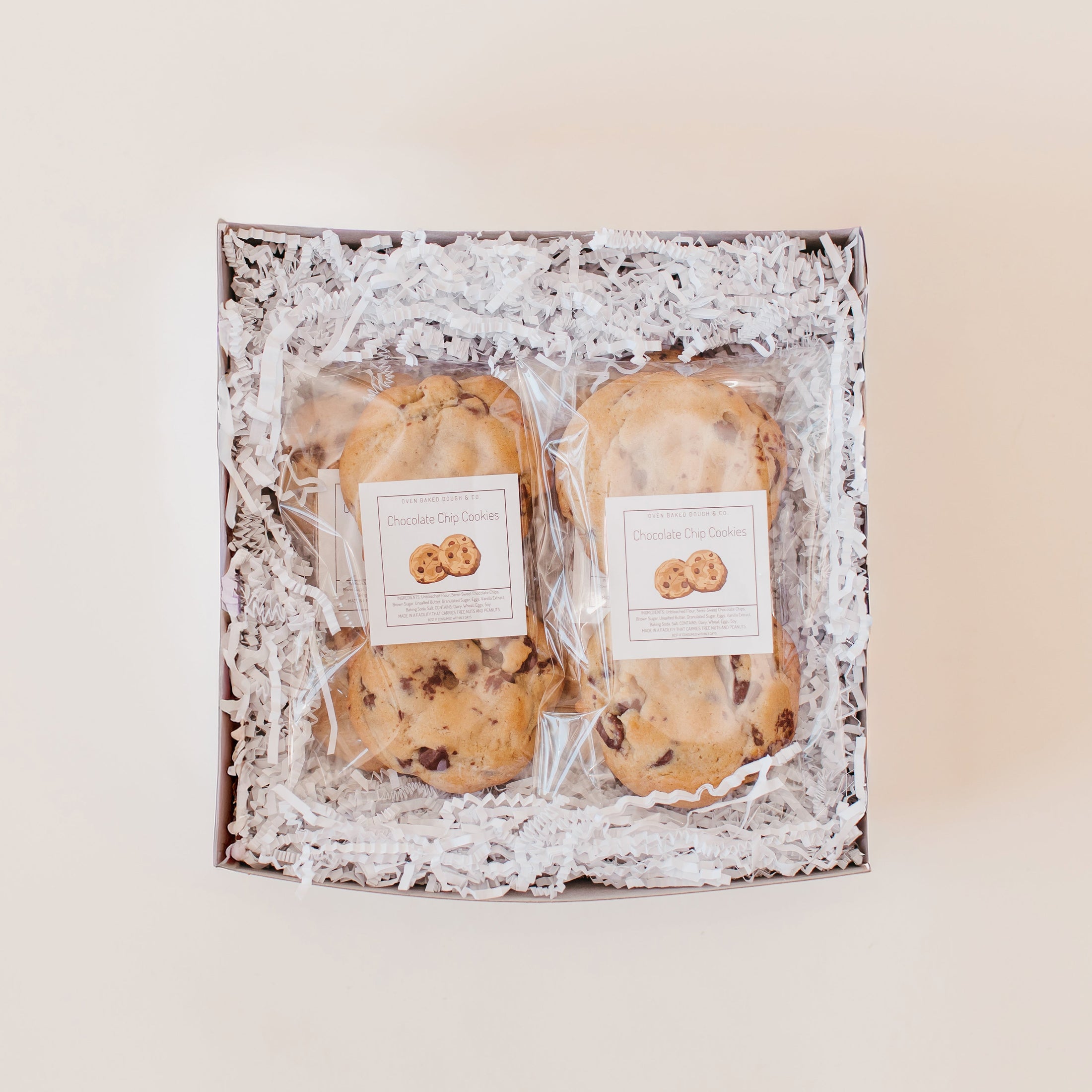 Chocolate chip cookies packaged in clear bags in a white gift box with white paper filler