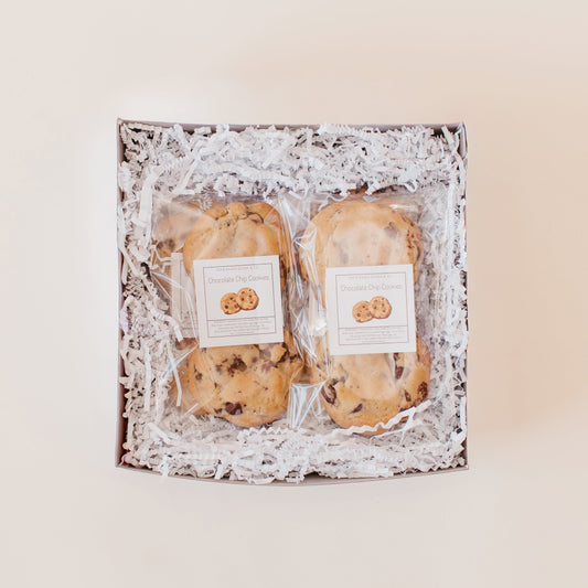 Chocolate chip cookies packaged in clear bags in a white gift box with white paper filler