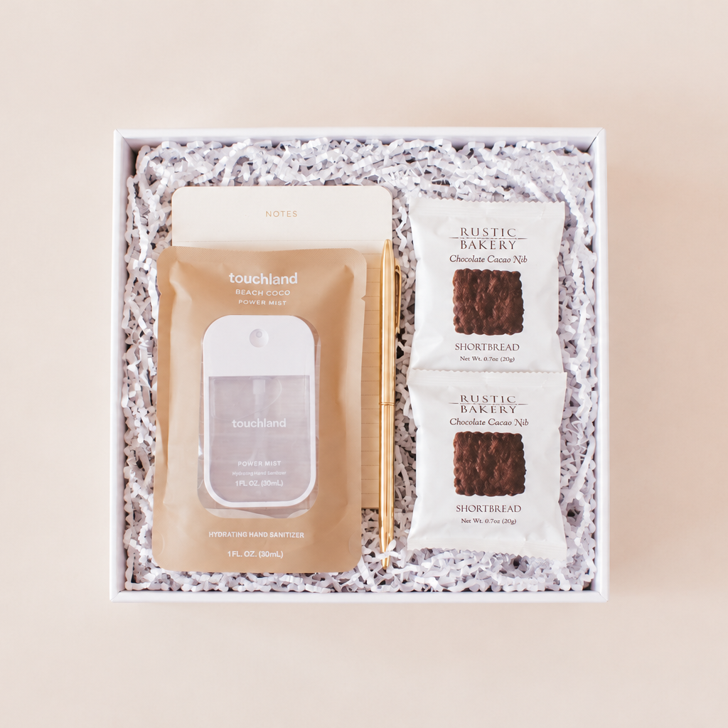 Desk essentials corporate gift box with Touchland Beach Coco hand sanitizer, notepad, gold pen, and Rustic Bakery chocolate shortbread in a white box with crinkle paper.