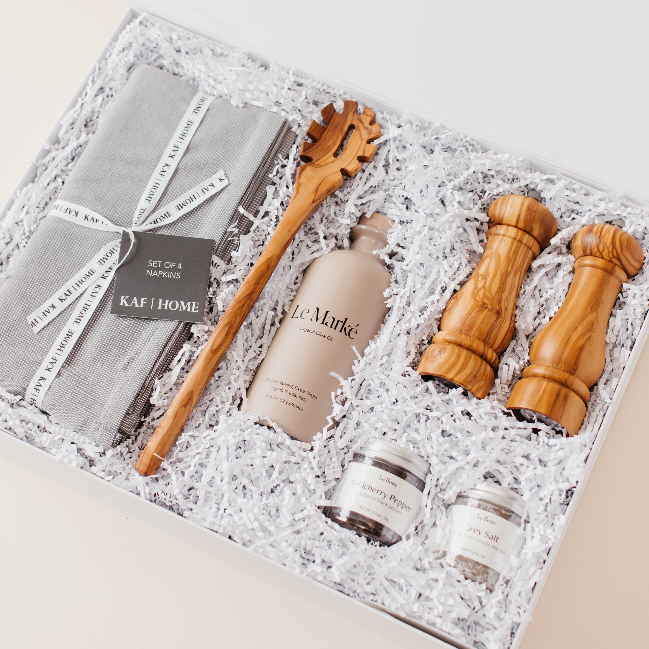 Lavender and Pine Entertainer's Kitchen Gift Box angle view featuring Kaf Home grey linen napkins, Le Marké olive oil, Natural OliveWood pasta spoon, Natural OliveWood salt and pepper mills, and La Boite grey salt and Tellicherry pepper in white magnetic gift box