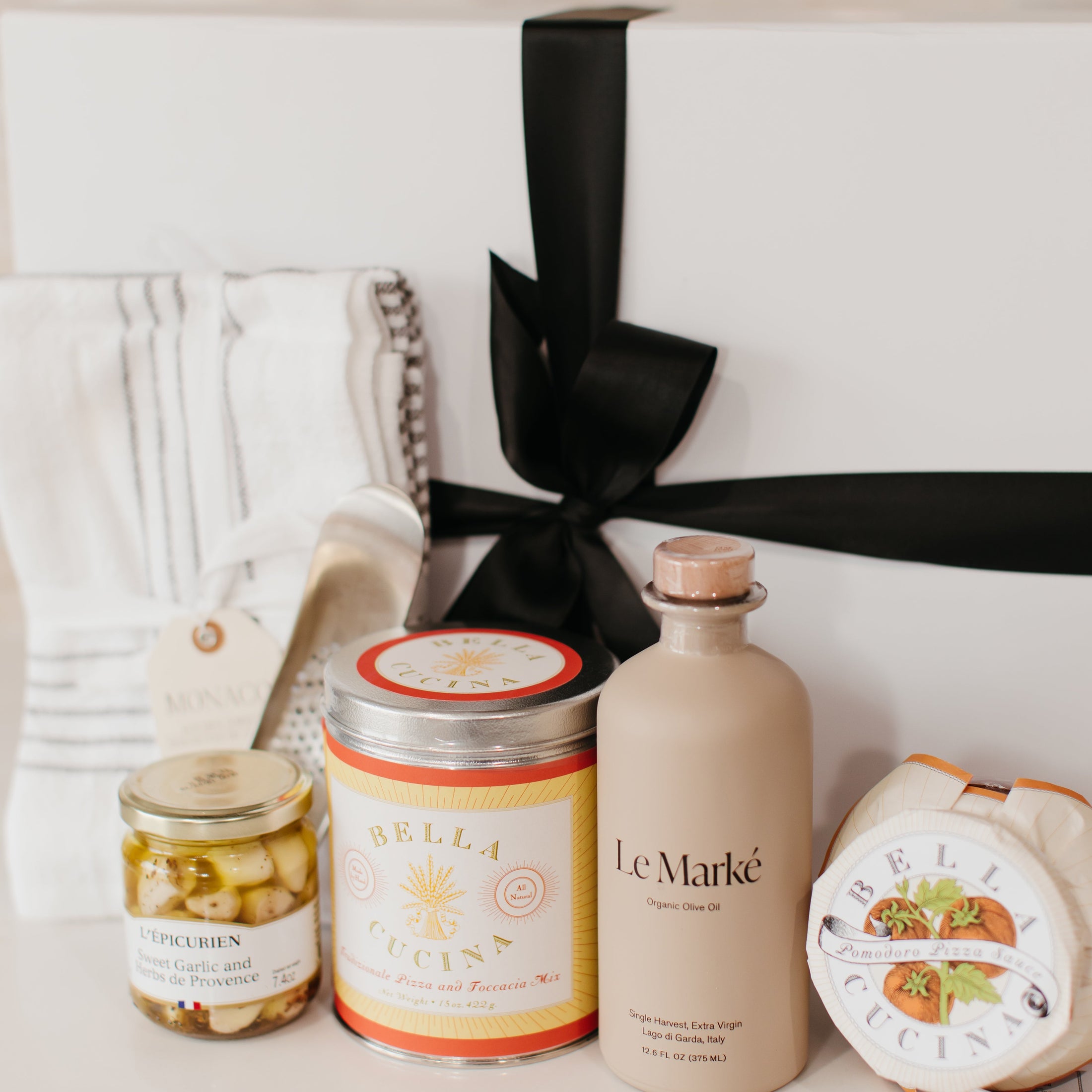Lavender and Pine Pizza Night Gift Box detail view featuring Le Marké olive oil, Bella Cucina pizza and focaccia mix, Bella Cucina pomodoro pizza sauce, French Farm L'Epicurien sweet garlic and herbs, stainless garlic rocker, and Kaf Home striped kitchen towel set in white magnetic gift box