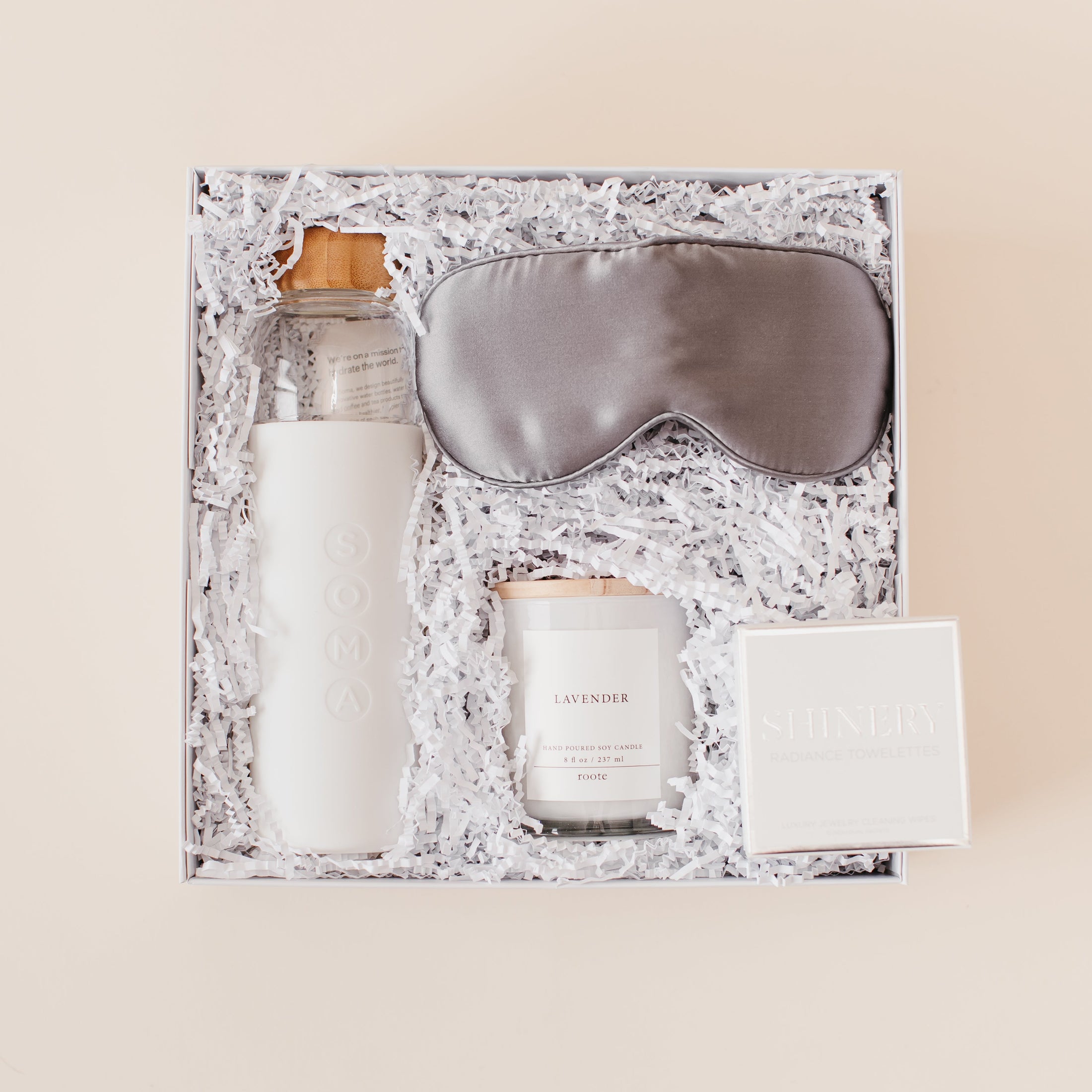 Lavender and Pine Rest and Restore Gift Box detail view featuring Soma glass water bottle, Pure Sol silk sleep mask, Roote lavender candle, and Shinery radiance towelettes in white luxe two piece gift box
