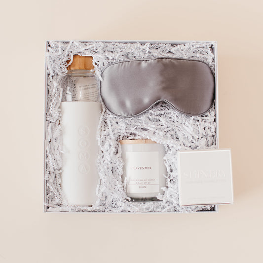 Lavender and Pine Rest and Restore Gift Box detail view featuring Soma glass water bottle, Pure Sol silk sleep mask, Roote lavender candle, and Shinery radiance towelettes in white luxe two piece gift box