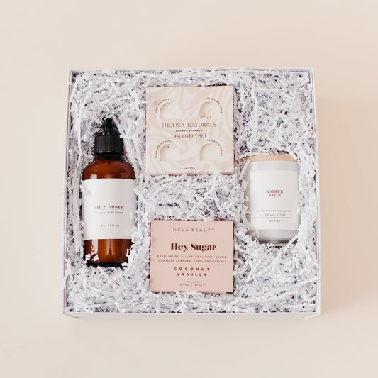 Lavender and Pine Self Care Sunday Gift Box featuring Roote oat and honey body lotion, Thulisa Naturals shower steamer discovery set, NCLA Beauty Hey Sugar coconut vanilla body scrub, and Roote Amber Noir candle in white luxe two piece gift box