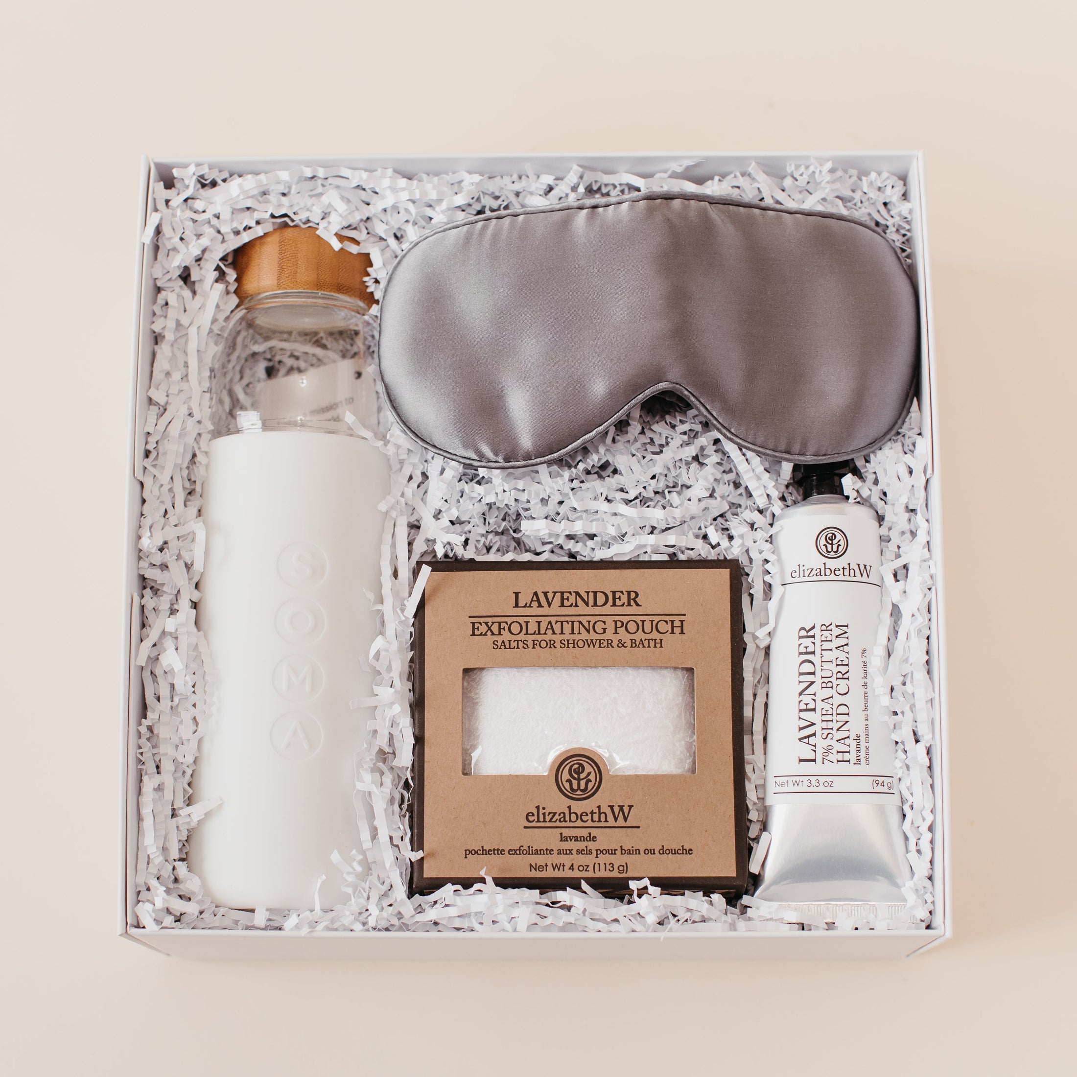 Lavender and Pine Soft Reset Gift Box featuring Soma glass water bottle, Pure Sol silk sleep mask, ElizabethW lavender exfoliating shower pouch, and ElizabethW lavender shea butter hand cream in white luxe two piece gift box