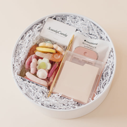 Lavender and Pine Desktop Edit gift box overhead angle featuring Scandy Candy Swedish candy, Touchland Rosewater Glow Mist, gold pen, and cream tabbed sticky notes in white round gift box