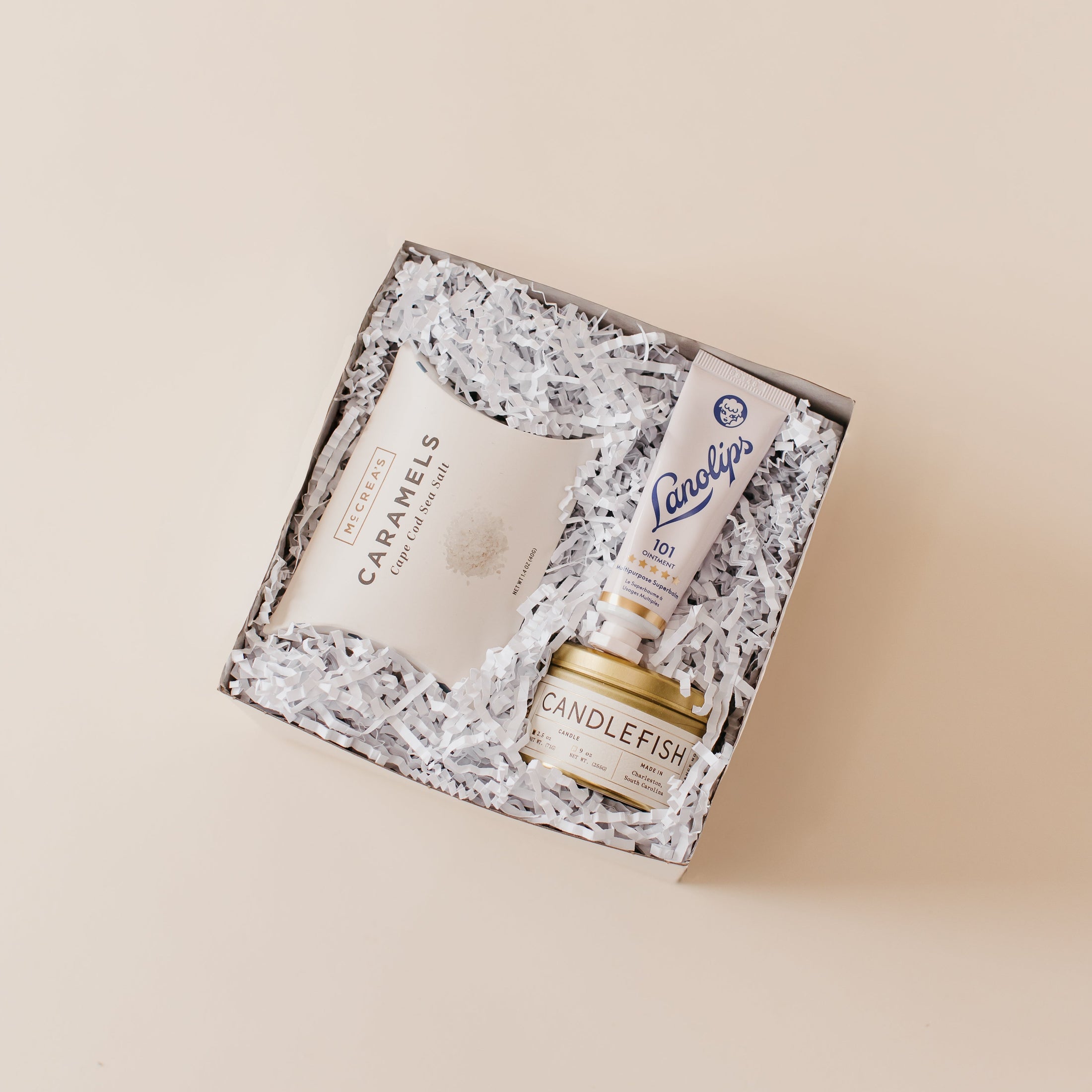 Lavender and Pine Ultimate Comfort Trio Gift Box angle view featuring Candlefish No. 31 candle tin, Lanolips 101 ointment, and McCrea's Cape Cod sea salt caramels in mini tuck top gift box