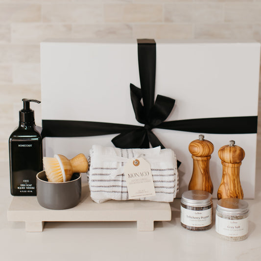 Lavender and Pine Well-Kept Kitchen Gift Box front view featuring Homecourt Cece dish soap, dish brush set, Monaco kitchen towels, Natural OliveWood salt and pepper mills, La Boite Tellicherry pepper and grey salt, and Luxe B Co sandstone trivet riser in white magnetic gift box.