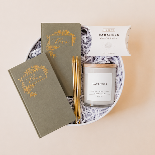 Lavender and Pine Written in Love Gift Box featuring Seniman Calligraphy olive vow books, gold ballpoint pens, Roote lavender candle, and McCrea's Cape Cod sea salt caramels in white round gift box